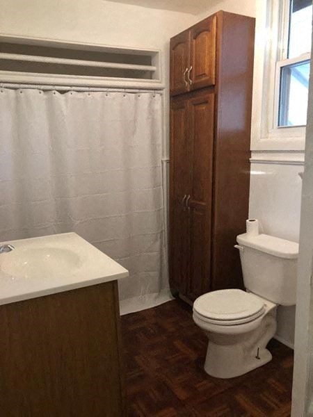 A white toilet sits in a bathroom next to a sink and a wooden cabinet.