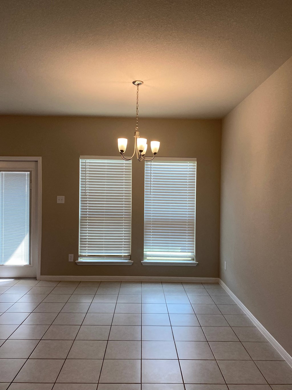 an empty living room with two windows and a chandelier