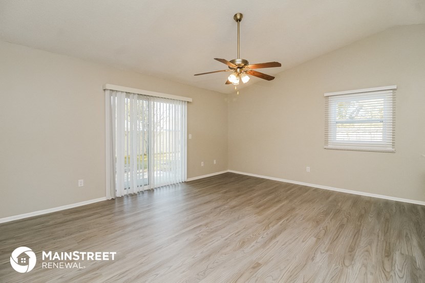 the spacious living room with wood flooring and a ceiling fan