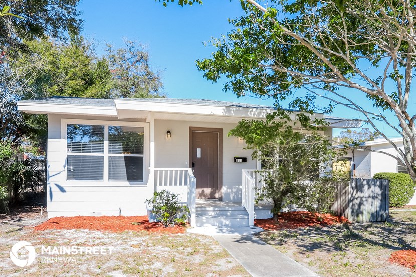 a small white house with a porch and a tree