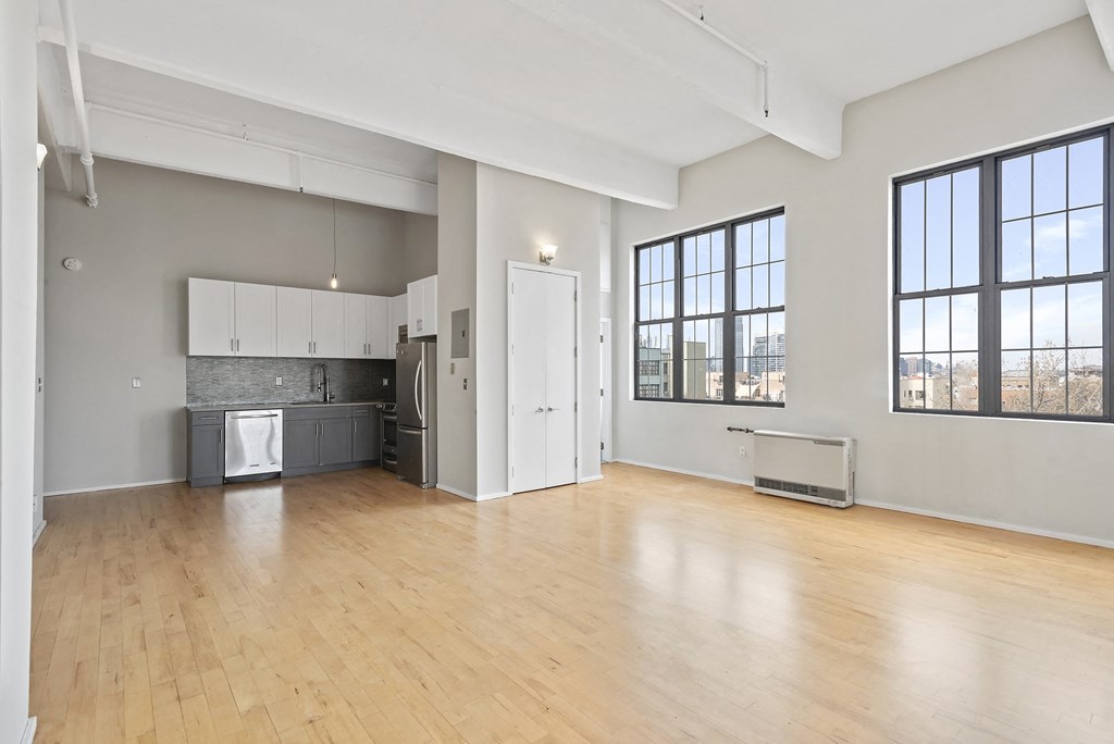an empty living room with a kitchen and a large window