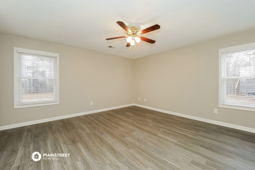 the spacious living room with hardwood flooring and a ceiling fan