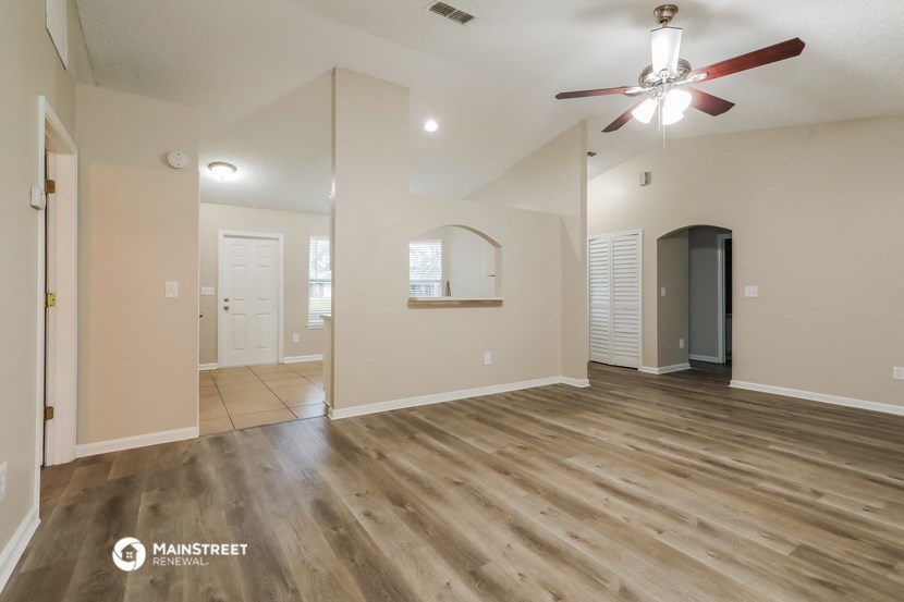 the spacious living room with hardwood flooring and a ceiling fan