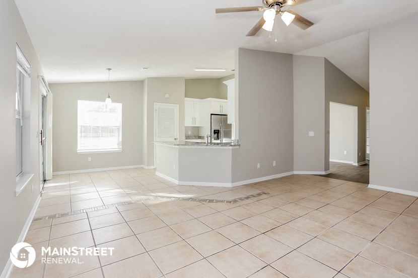 an empty living room with a kitchen and a ceiling fan