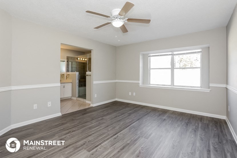 the spacious living room with wood flooring and a ceiling fan
