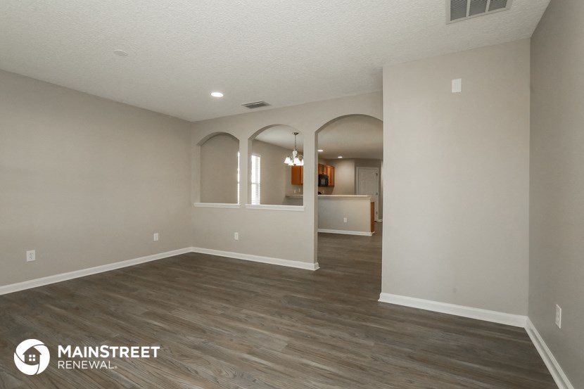the spacious living room and dining room with white walls and wood flooring