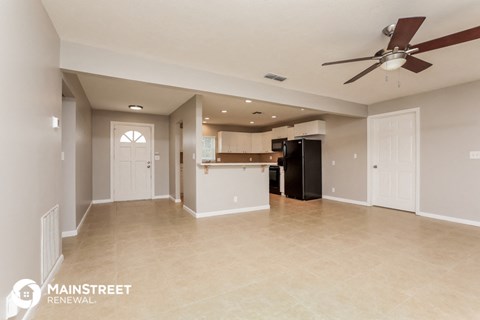 an empty living room with a kitchen and a ceiling fan