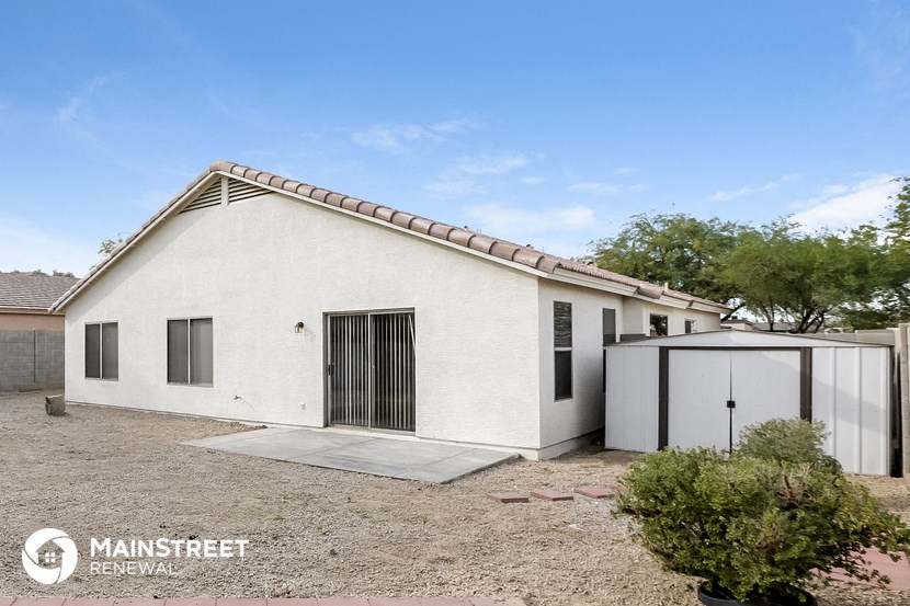 a small white house with a garage and a dirt yard