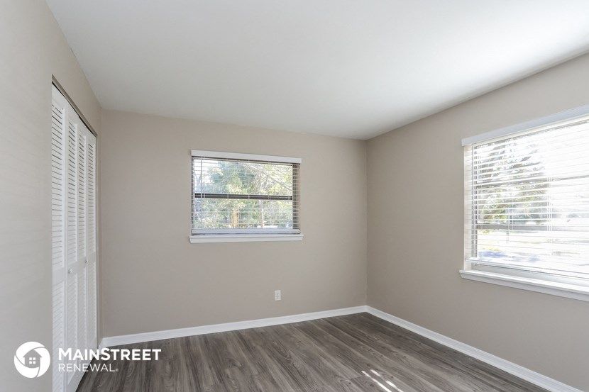 the interior of an empty room with wood flooring and two windows