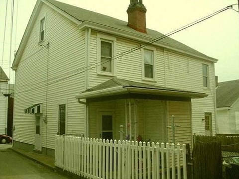 A white house with a brown roof and a white picket fence.
