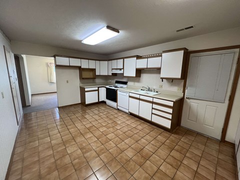 A kitchen with brown tiles and white cabinets.