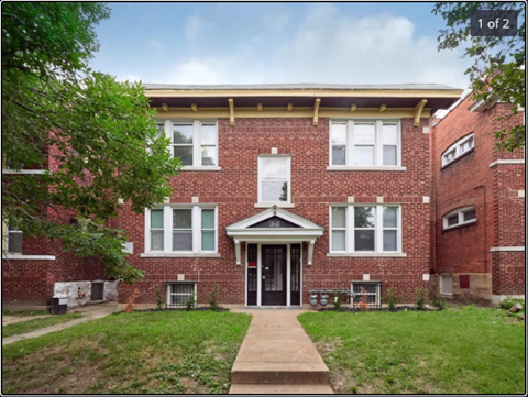 the front of a brick apartment building with a sidewalk and grass