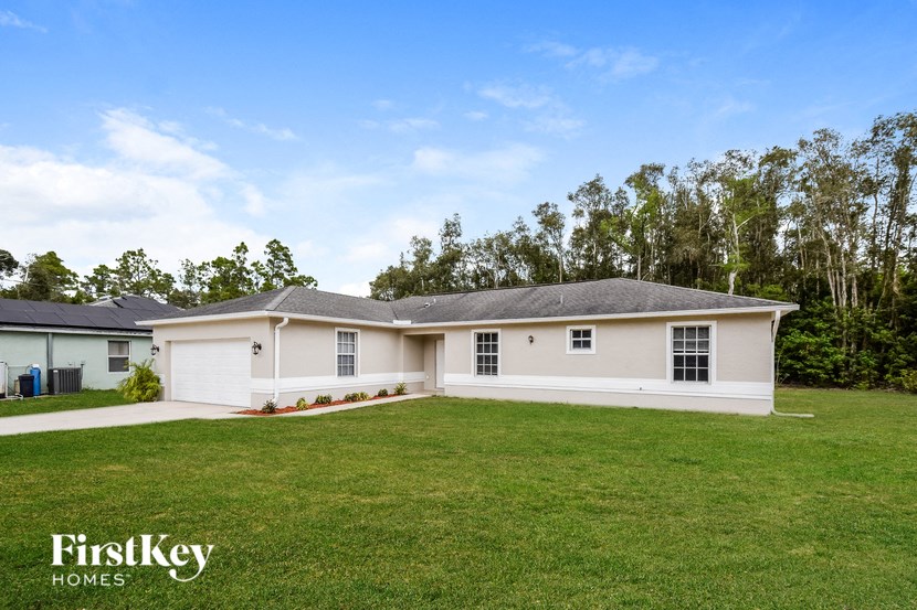 A white house with a grey roof is surrounded by a green lawn.