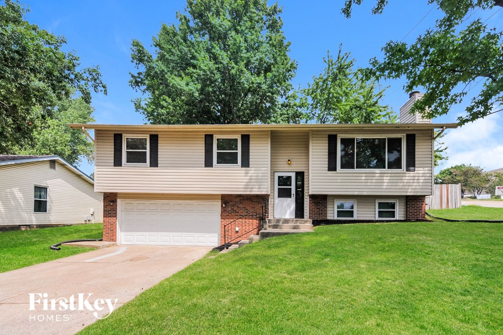 a beige and brick house with a lawn and trees