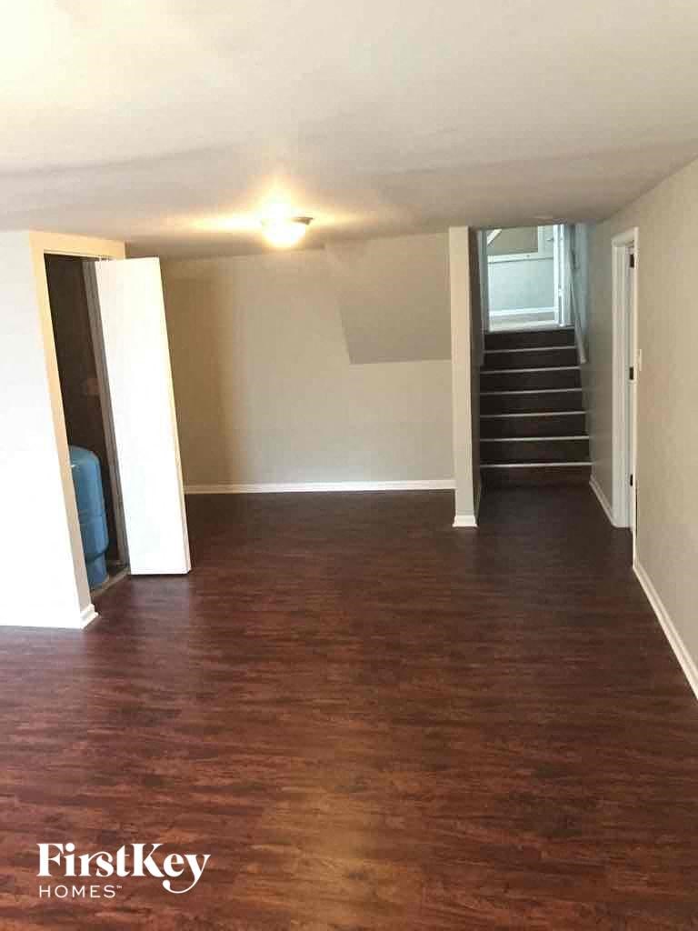A room with wooden floors and a staircase in the background.