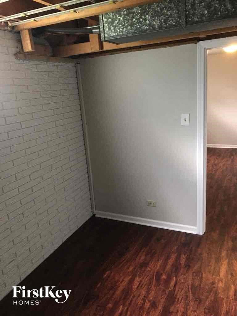 A small white refrigerator in a room with wooden floors and a brick wall.