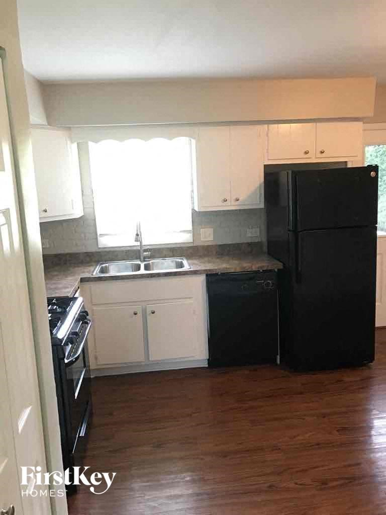 A black refrigerator stands in a kitchen with white cabinets.