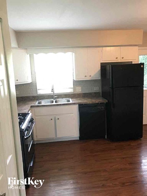 A black refrigerator stands in a kitchen with white cabinets.