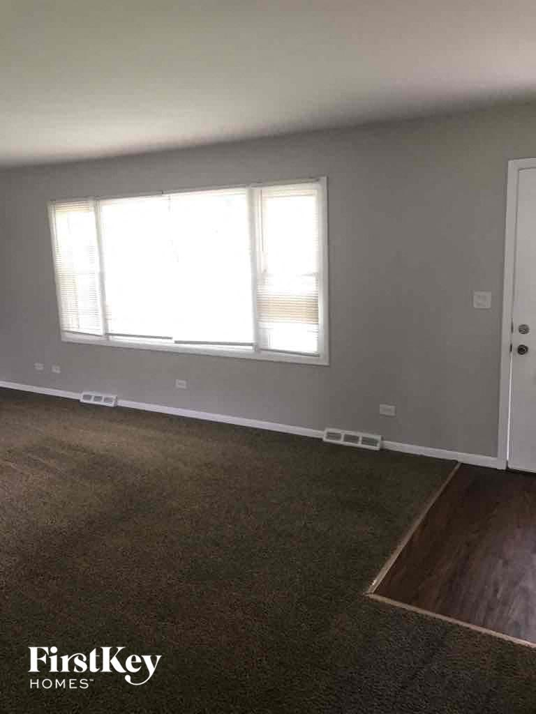 A room with a carpeted floor, a door, and a window with blinds.