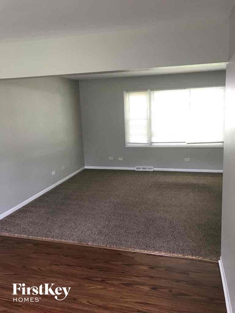 A room with a carpeted floor and a window with blinds.