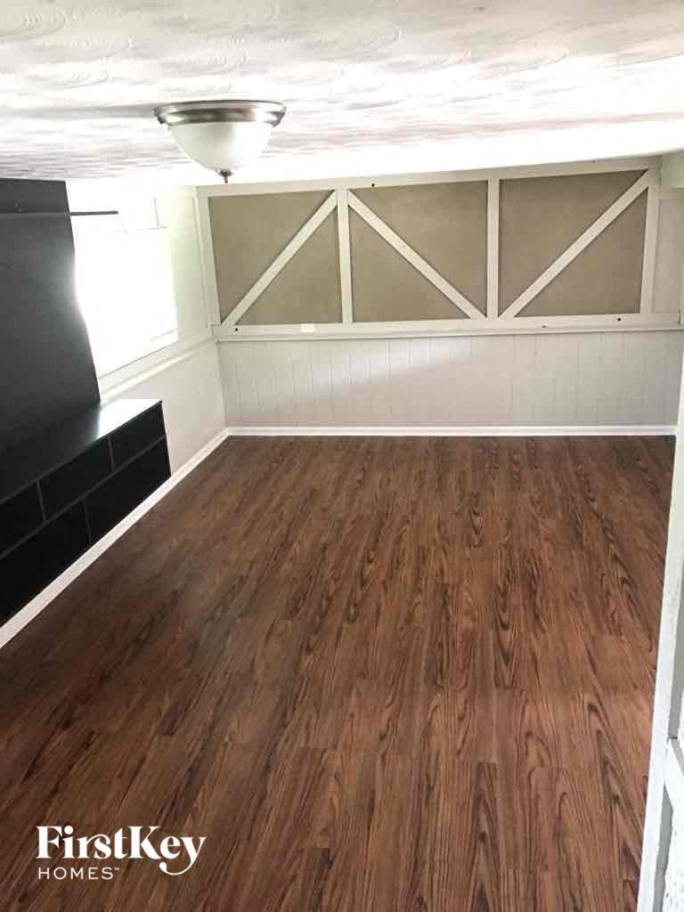 A room with wooden flooring and a white wall with a window.