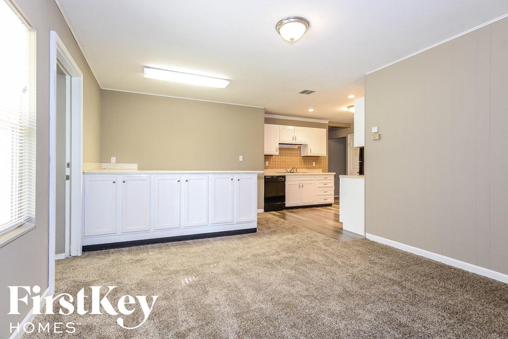 A spacious room with a kitchen area in the background and a carpet on the floor.