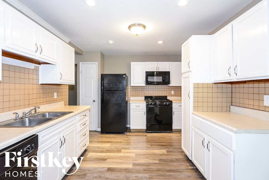 A kitchen with white cabinets and a black fridge.