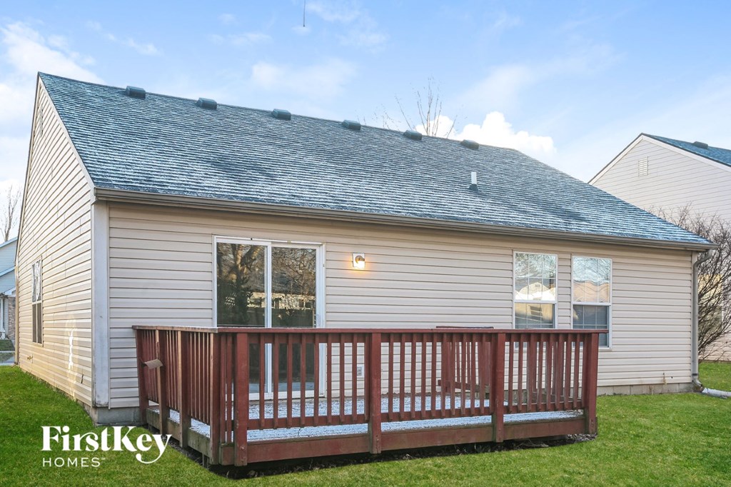 the backyard of a white house with a wooden deck