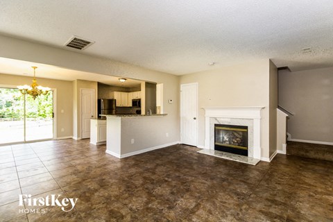 A large, empty living room with a fireplace and a kitchen in the background.