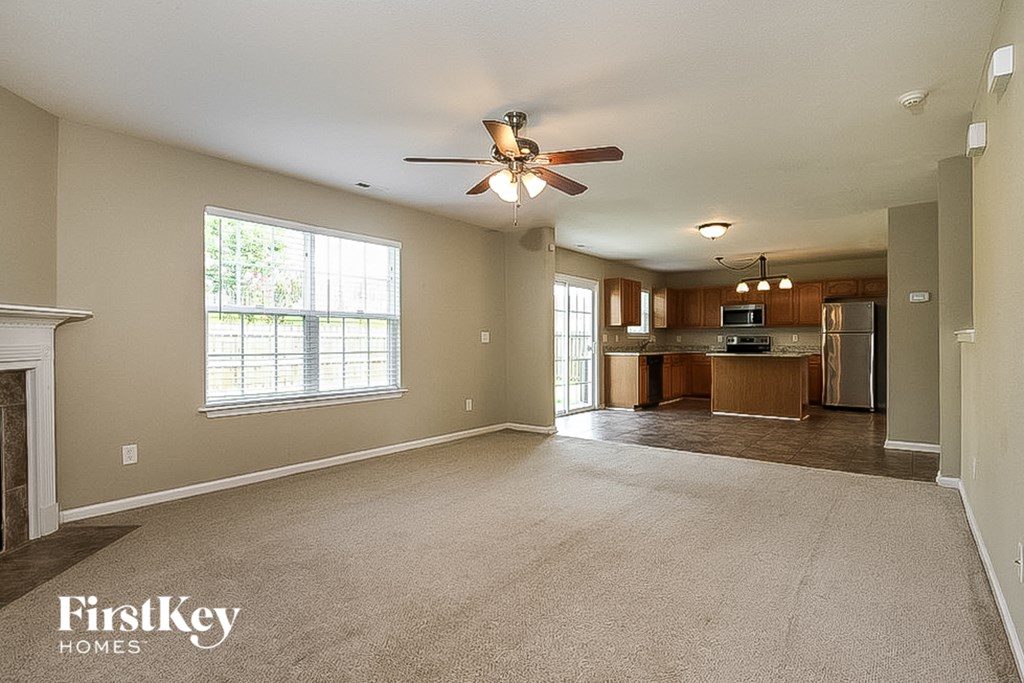 an empty living room with a ceiling fan and a kitchen