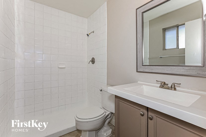 A white tiled bathroom with a toilet, sink and mirror.