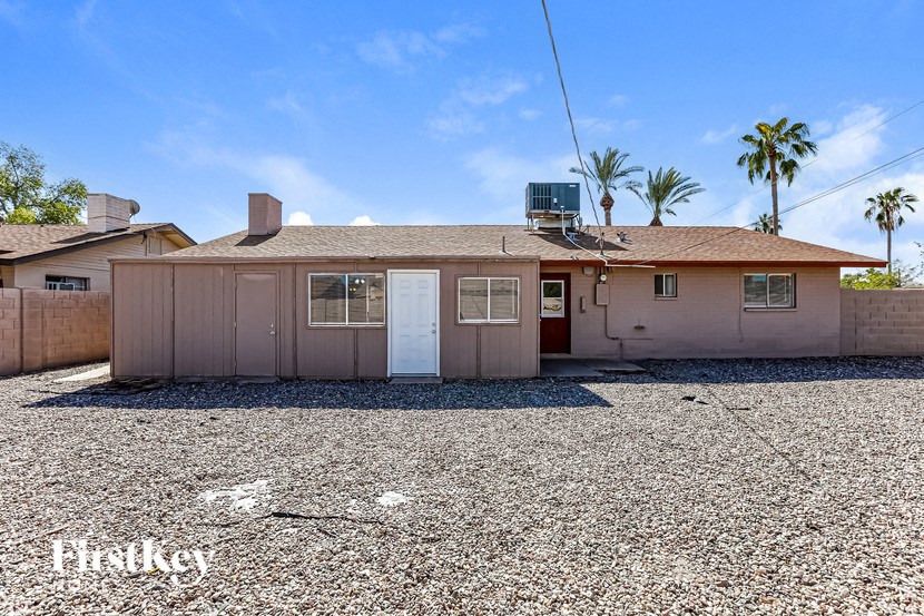 A house with a brown roof and a white door is surrounded by a gravel lot.