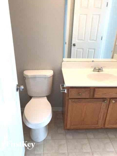 A white toilet in a bathroom with a white sink and wooden cabinet.