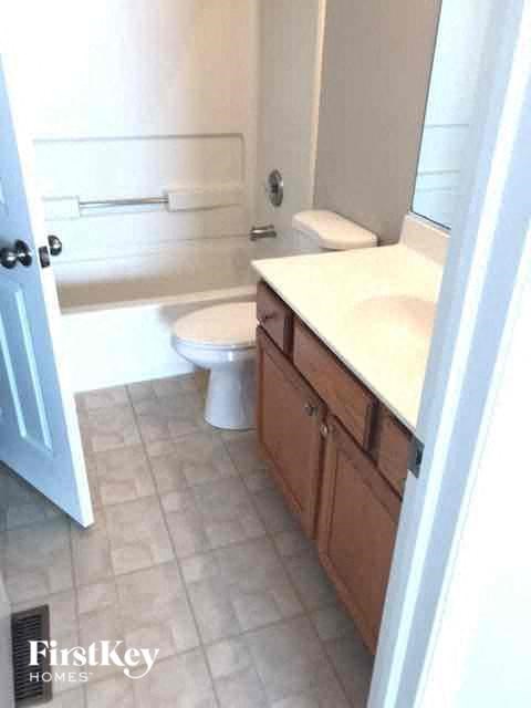 A white toilet sits in a bathroom with a white sink and wooden cabinets.