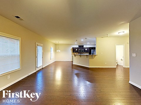 an empty living room with a kitchen in the background