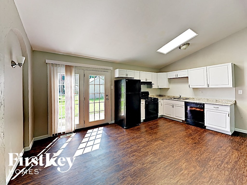an empty kitchen with white cabinets and black appliances and wood floors