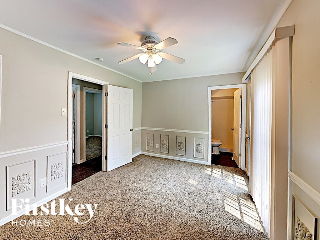 an empty bedroom with a ceiling fan and a door to the bathroom