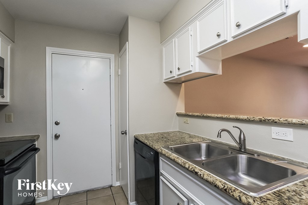 a kitchen with a sink and white cabinets and a white door
