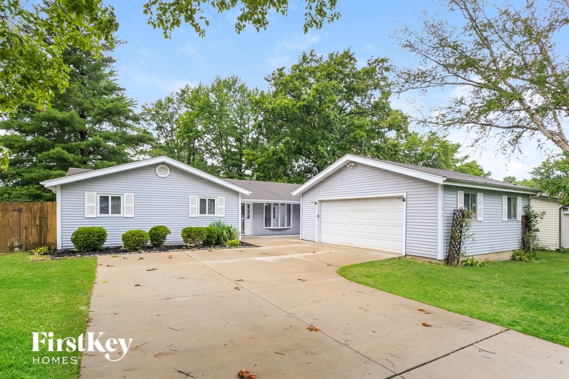a blue and white house with a driveway and trees
