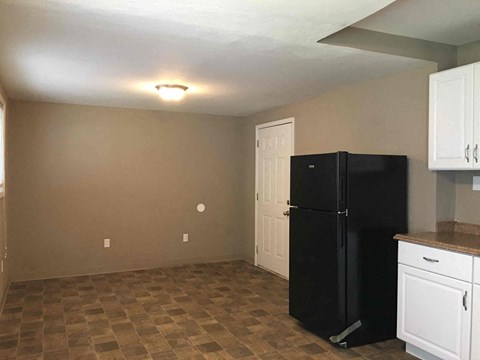 A black refrigerator sits in a kitchen with white cabinets and a checkered floor.