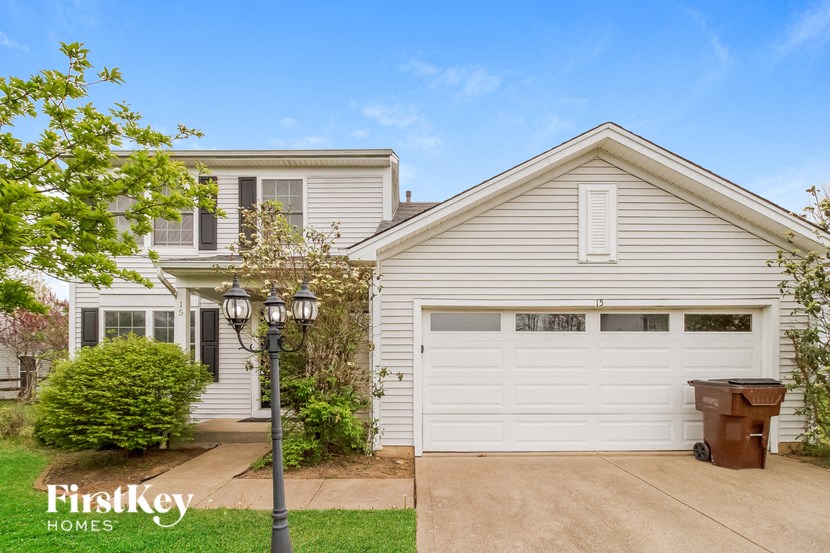 A house with a white garage door and a brown trash can in front of it.