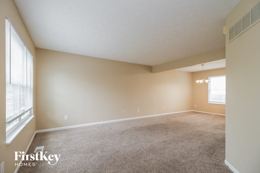 A spacious room with a carpeted floor and a window on the left side.