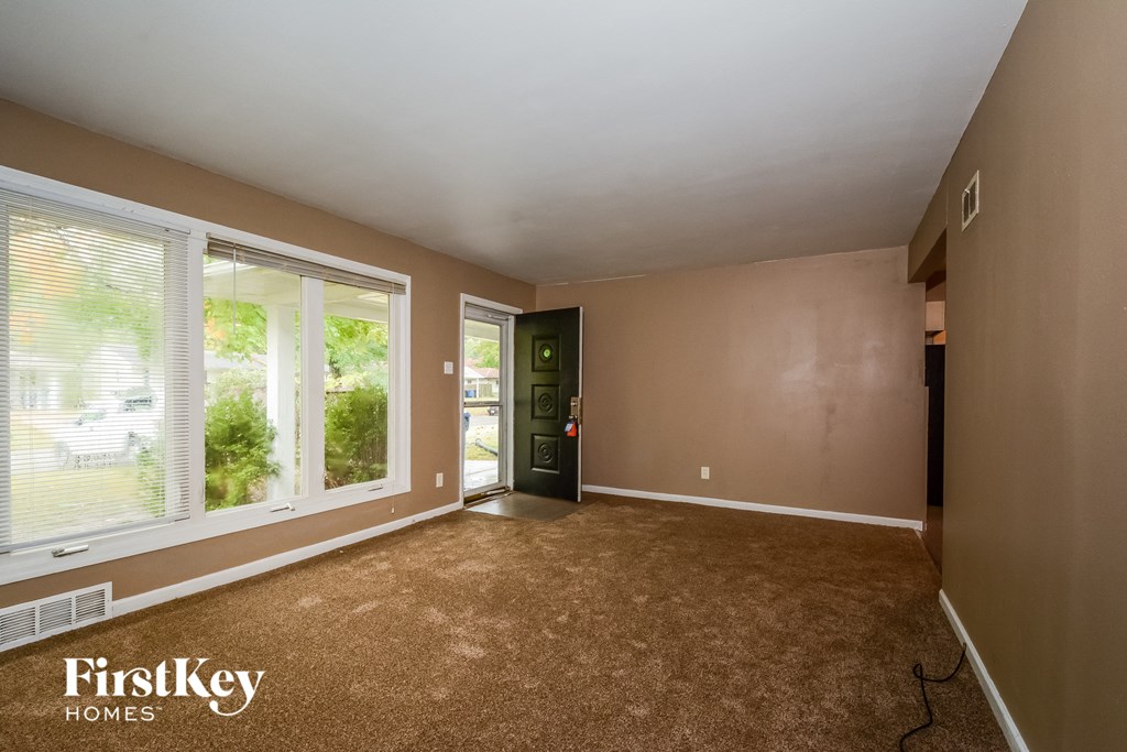 the living room of a house with a carpeted floor and large windows