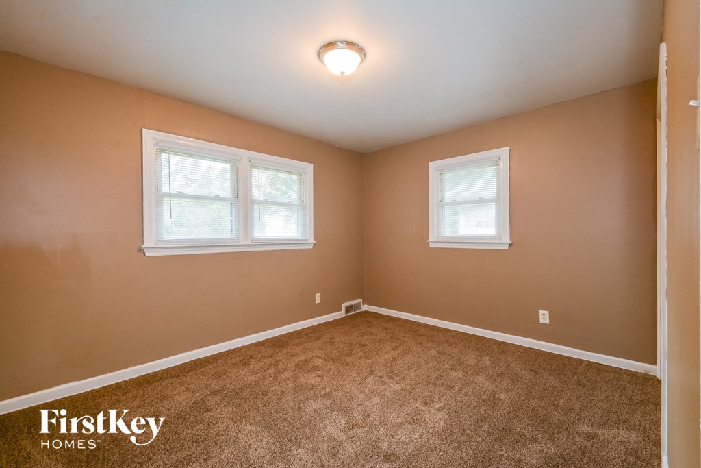 the bedroom of a house with carpet and two windows
