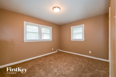 the bedroom of a house with carpet and two windows
