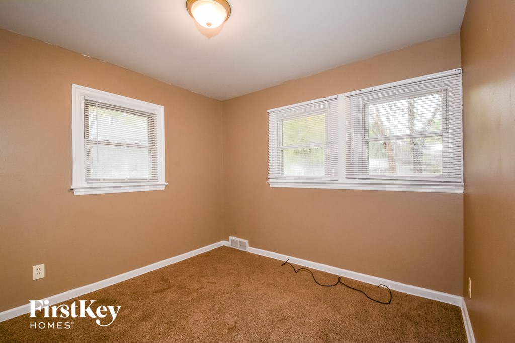 the bedroom of a house with carpet and two windows