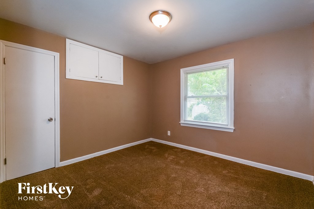 the bedroom of a house with brown carpet and a window