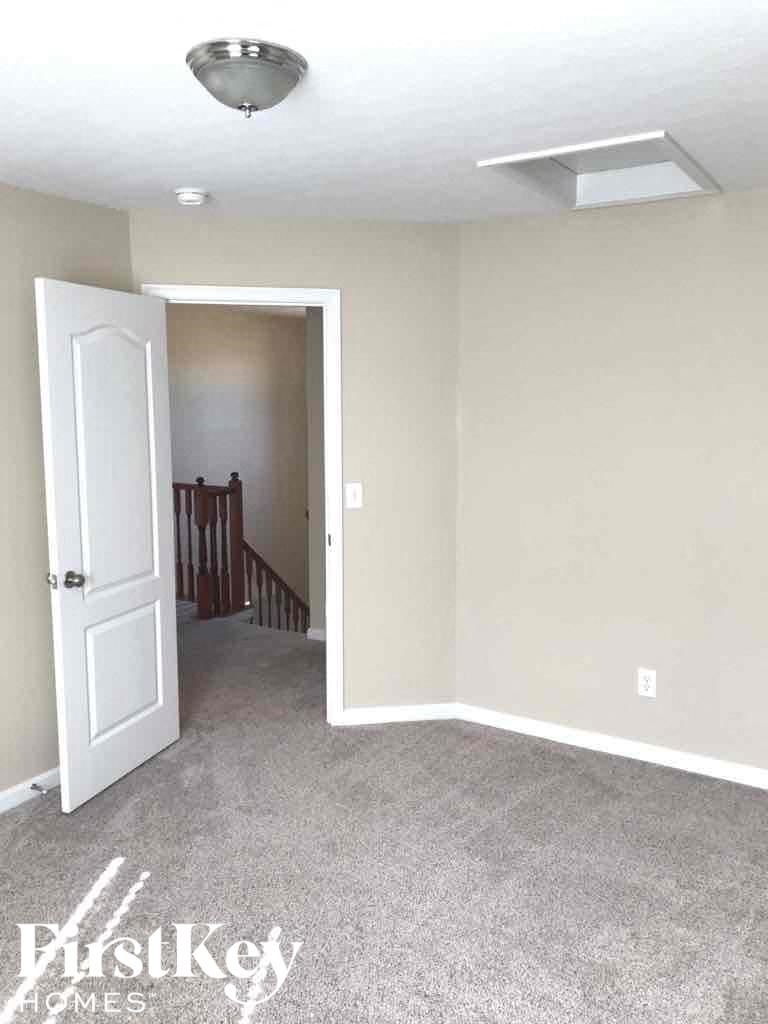 an empty carpeted living room with a white door and a staircase