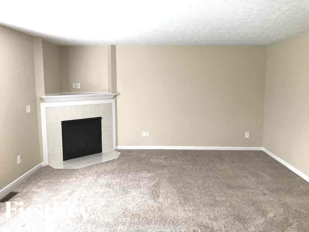 an empty living room with a fireplace and carpeted floor