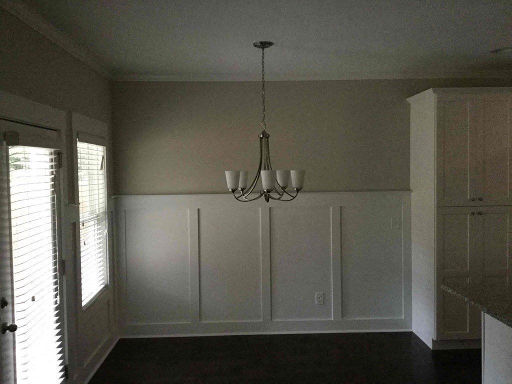 A chandelier hangs from the ceiling in a room with white walls and a dark floor.